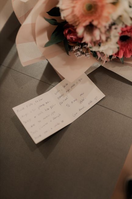 A floral arrangement of fresh flowers featuring pink and white blooms, possibly roses and carnations, with green foliage arranged in a compact bouquet. The bouquet is wrapped in soft pastel pink tissu